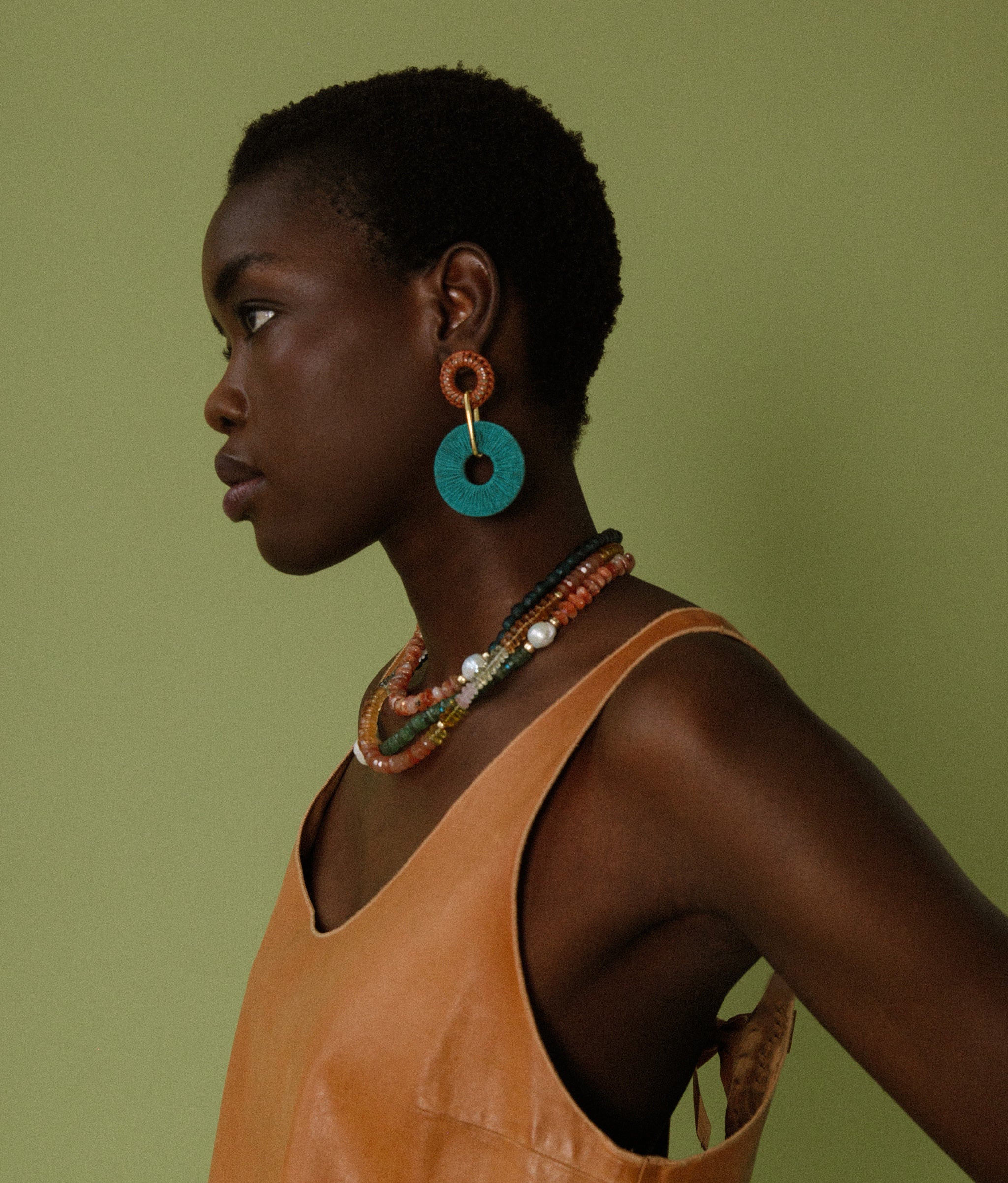 Model on green backdrop wears orange top with New Moon Earrings, Selena Necklace and Cabana Necklace in Terra.