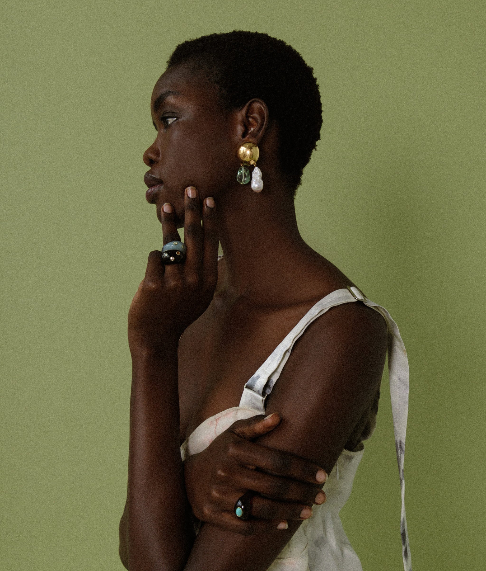 Model on green backdrop wears floral dress, Cascada Earrings, and assorted Monument Rings.
