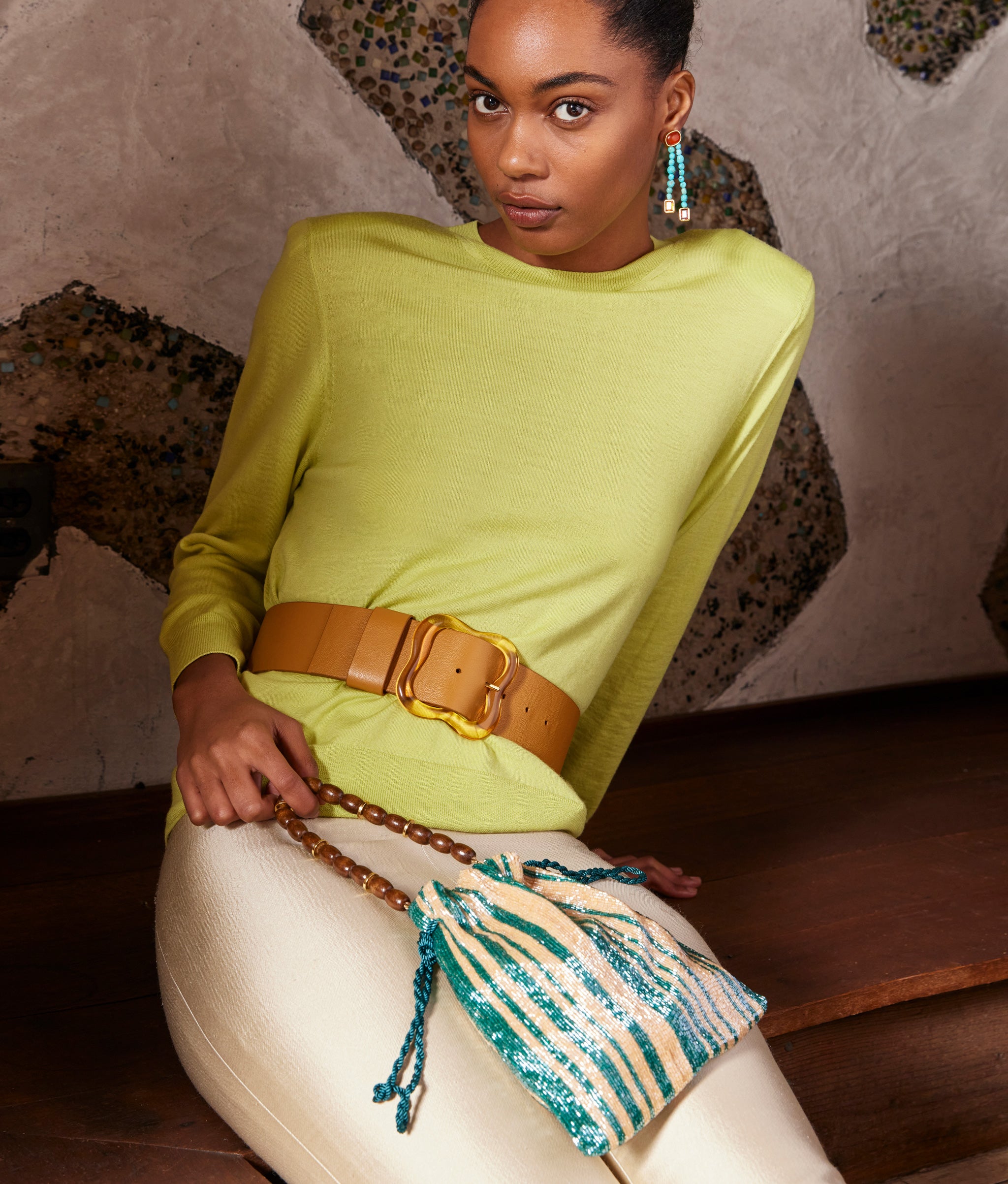 Model in chartreuse top wears Florence Belt in Amber and holds Gala Bag in Disco Stripe.