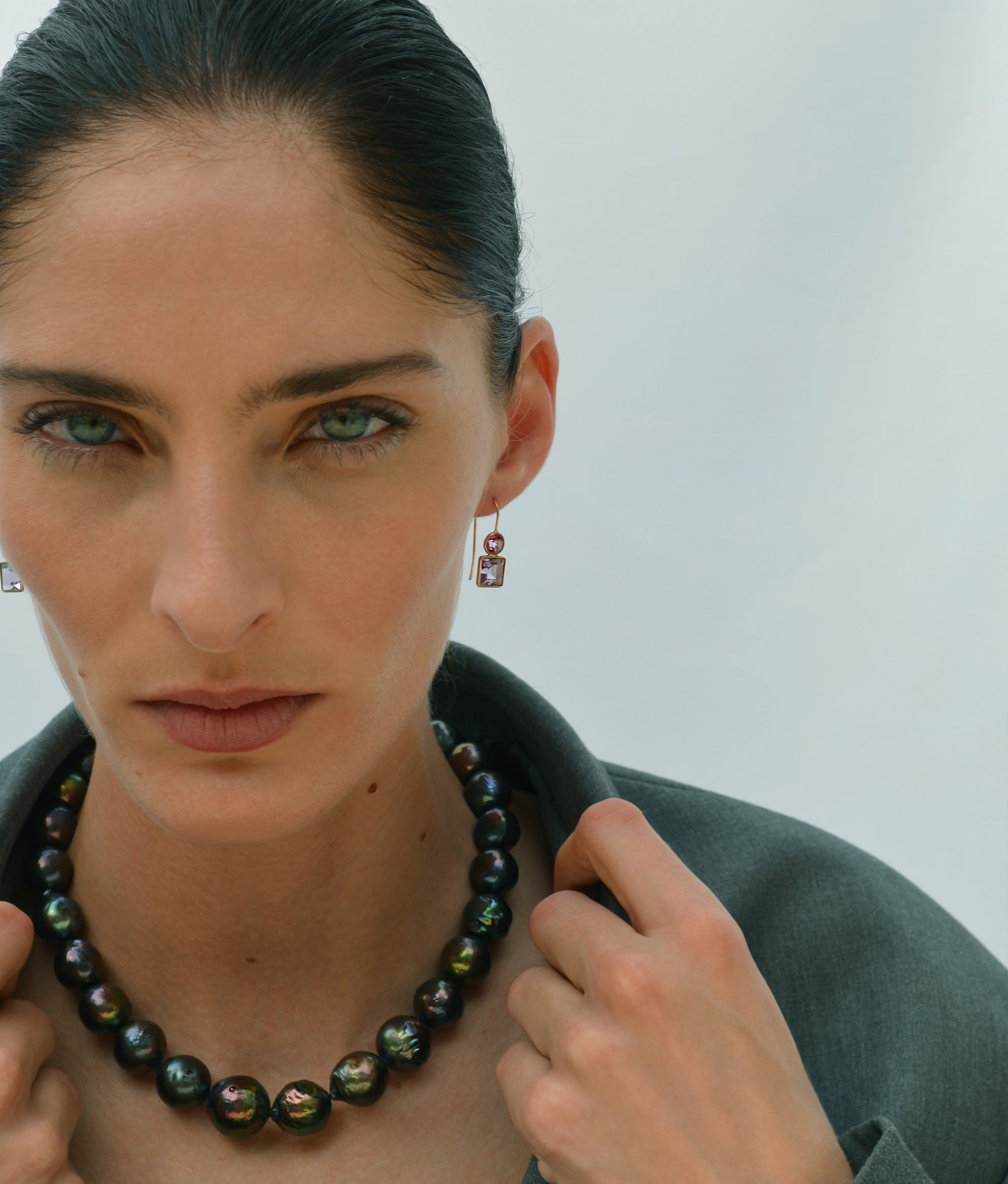 Model on blue backdrop wears green top with Peacock Baroque Pearl Necklace and Pastille Earrings