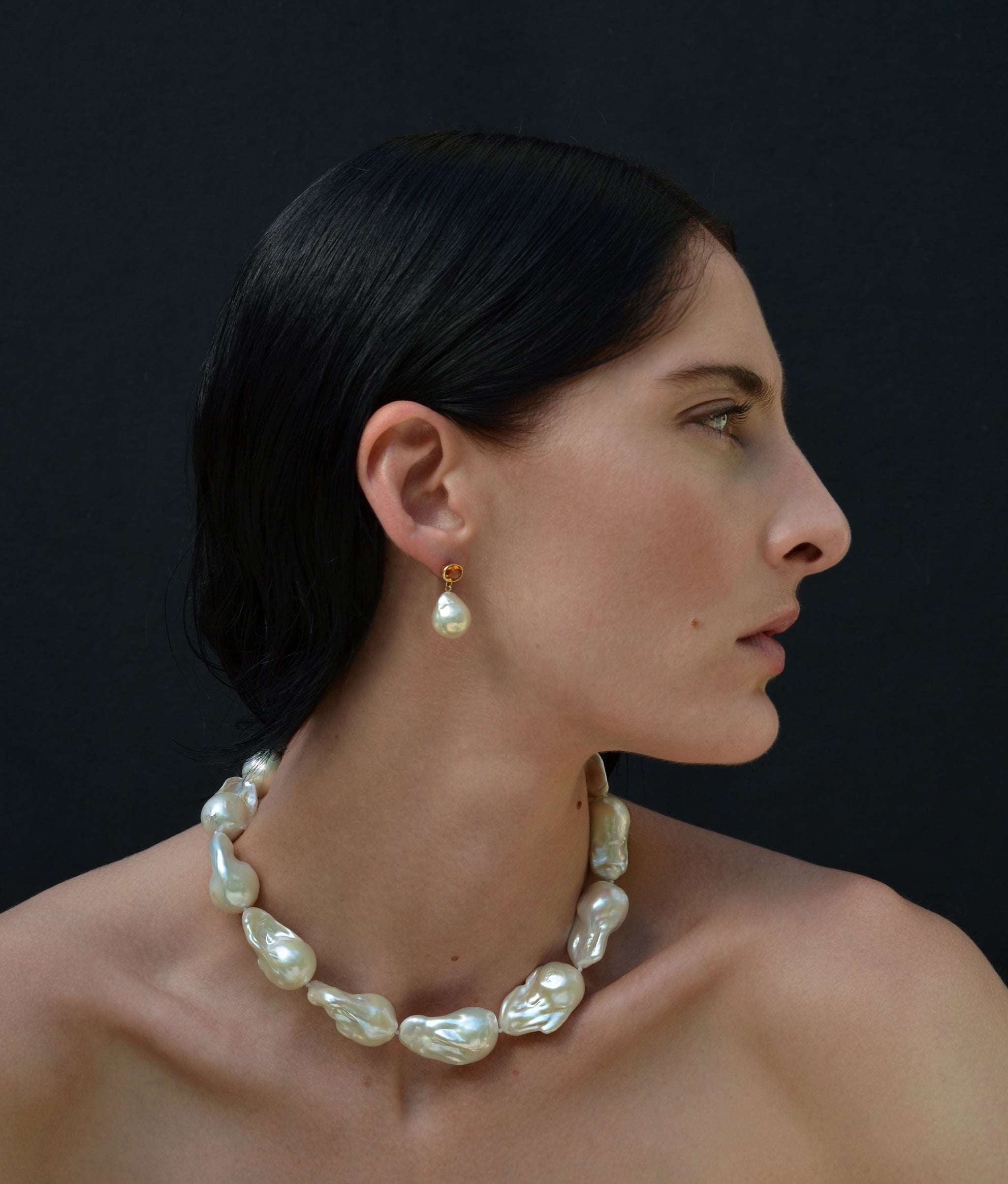 Model in profile on black backdrop wears Extra Large White Baroque Pearl Necklace with pearl earrings