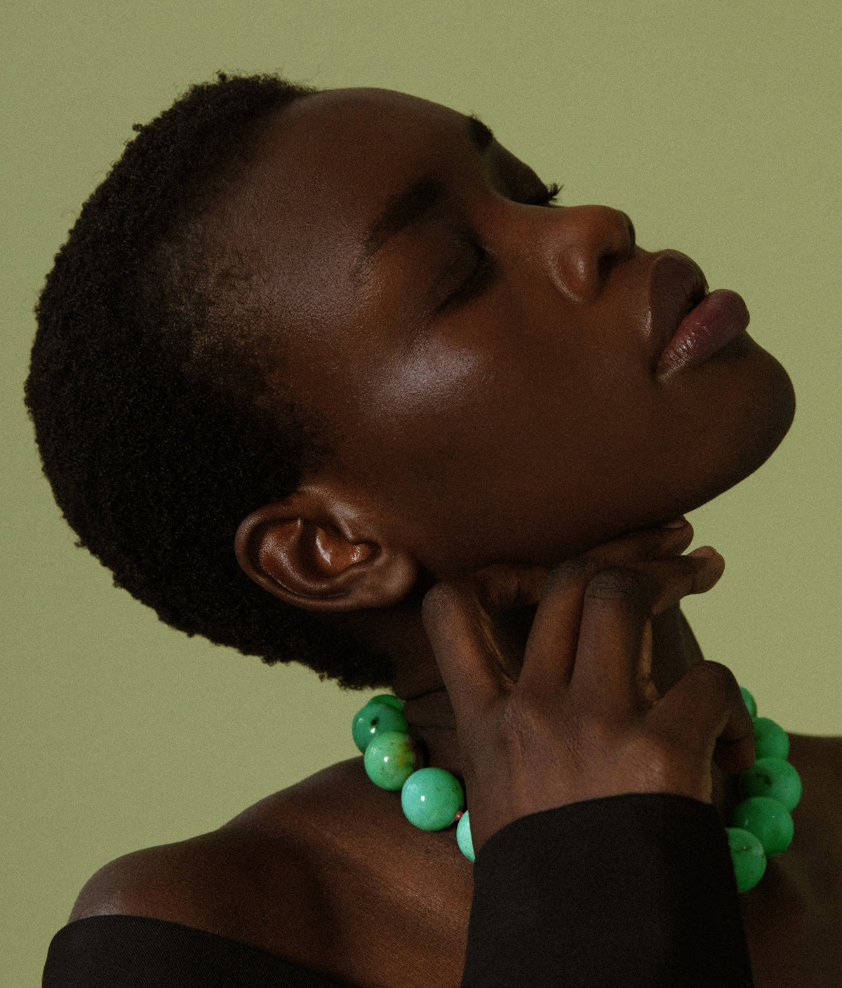 Model in profile on green backdrop wears Jumbo Chrysoprase, Ruby & 14k Gold Necklace. 