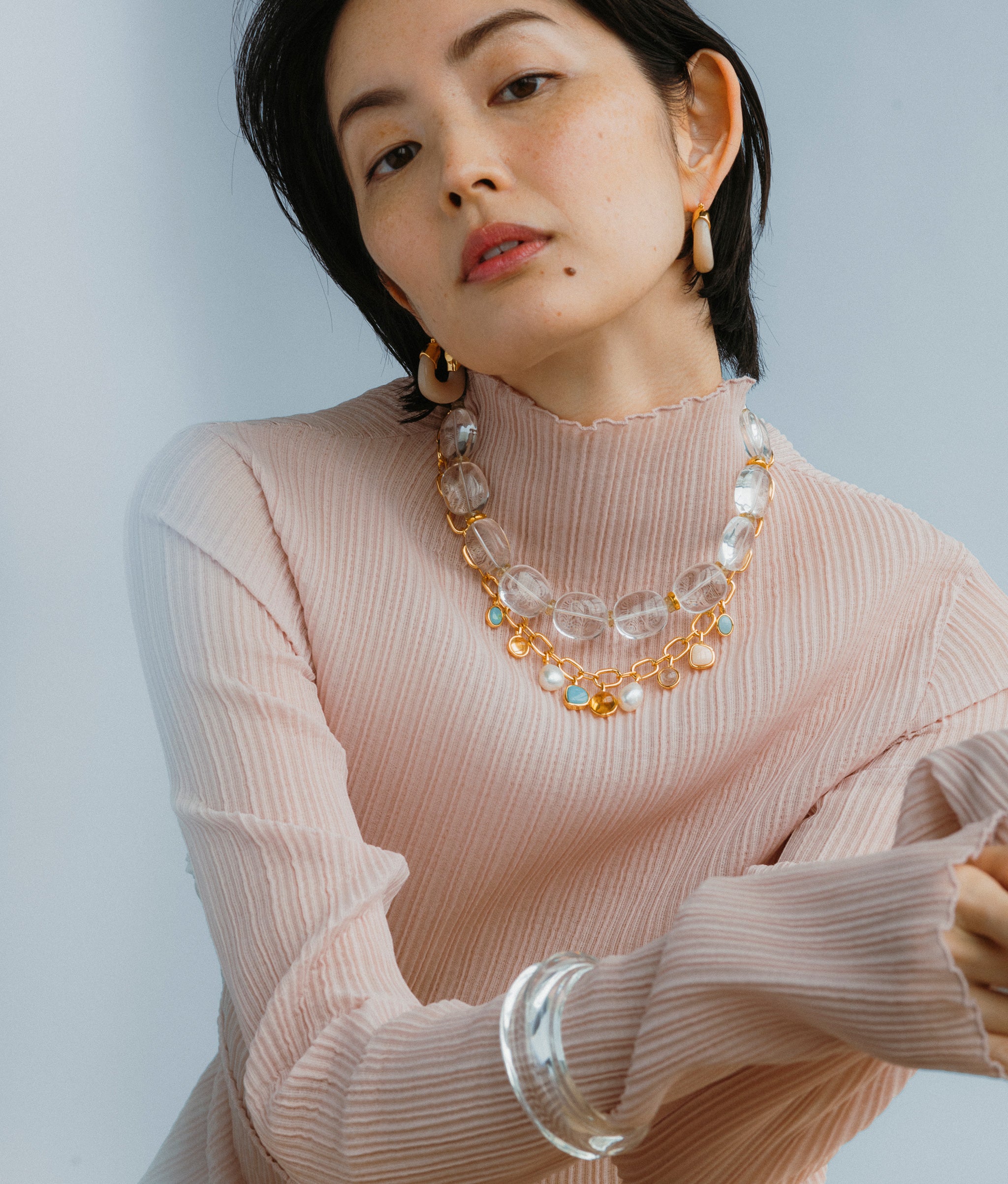 Model in a blue backdrop, wears  Mini Organic Hoops In Dove,  the Arabesque Necklace and Clear Ridge Cuff.