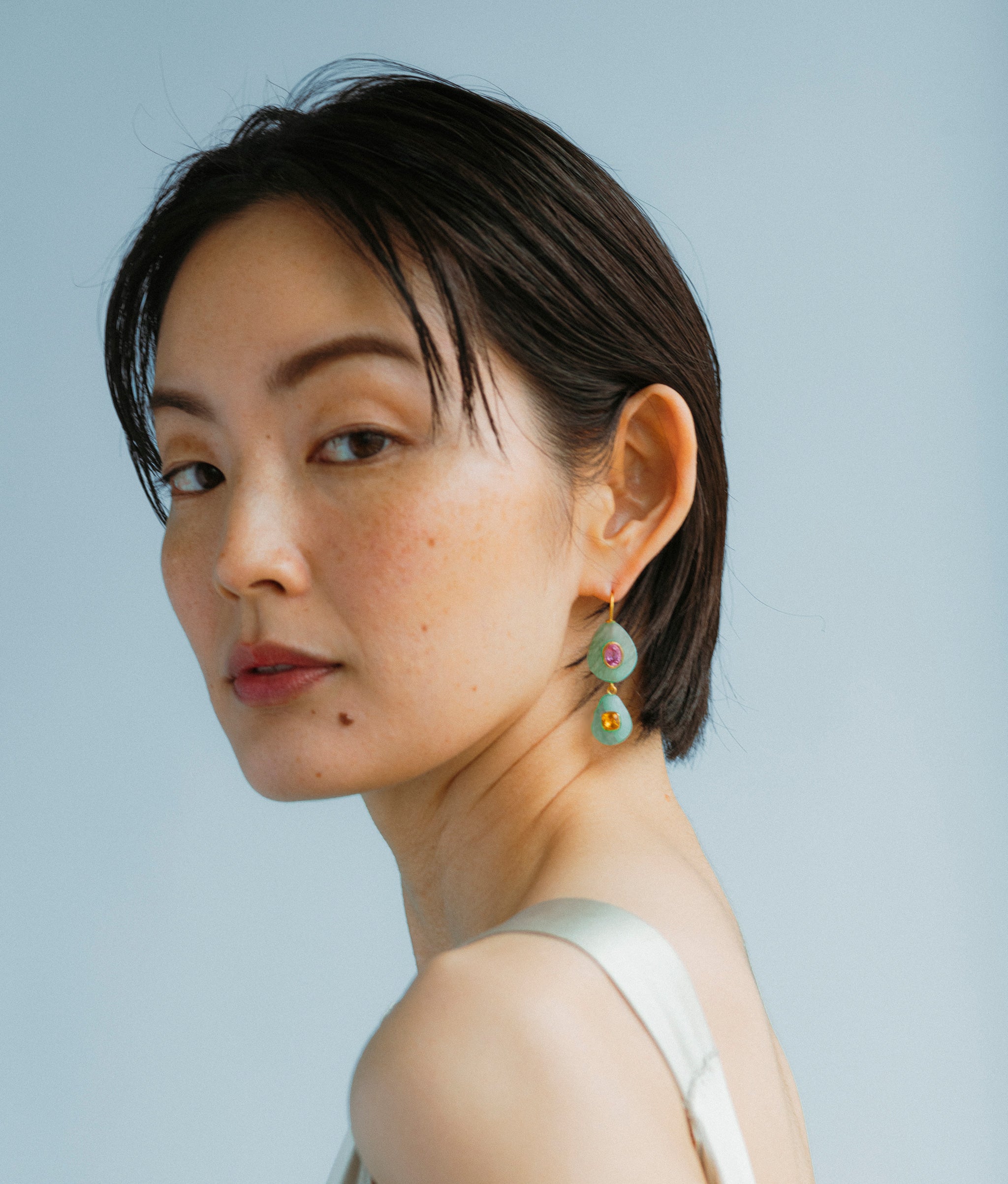 Model wears Stacked Stone Earrings In Amazonite in a blue backdrop.