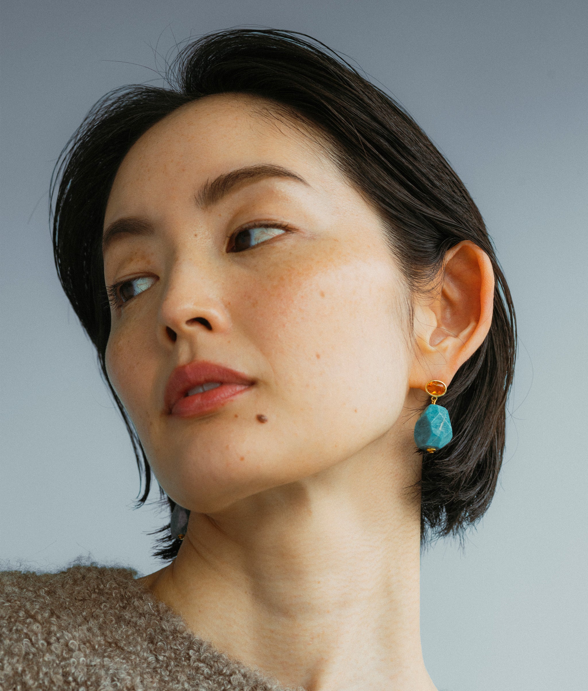 Model wears Galapagos Earrings on a blue backdrop.