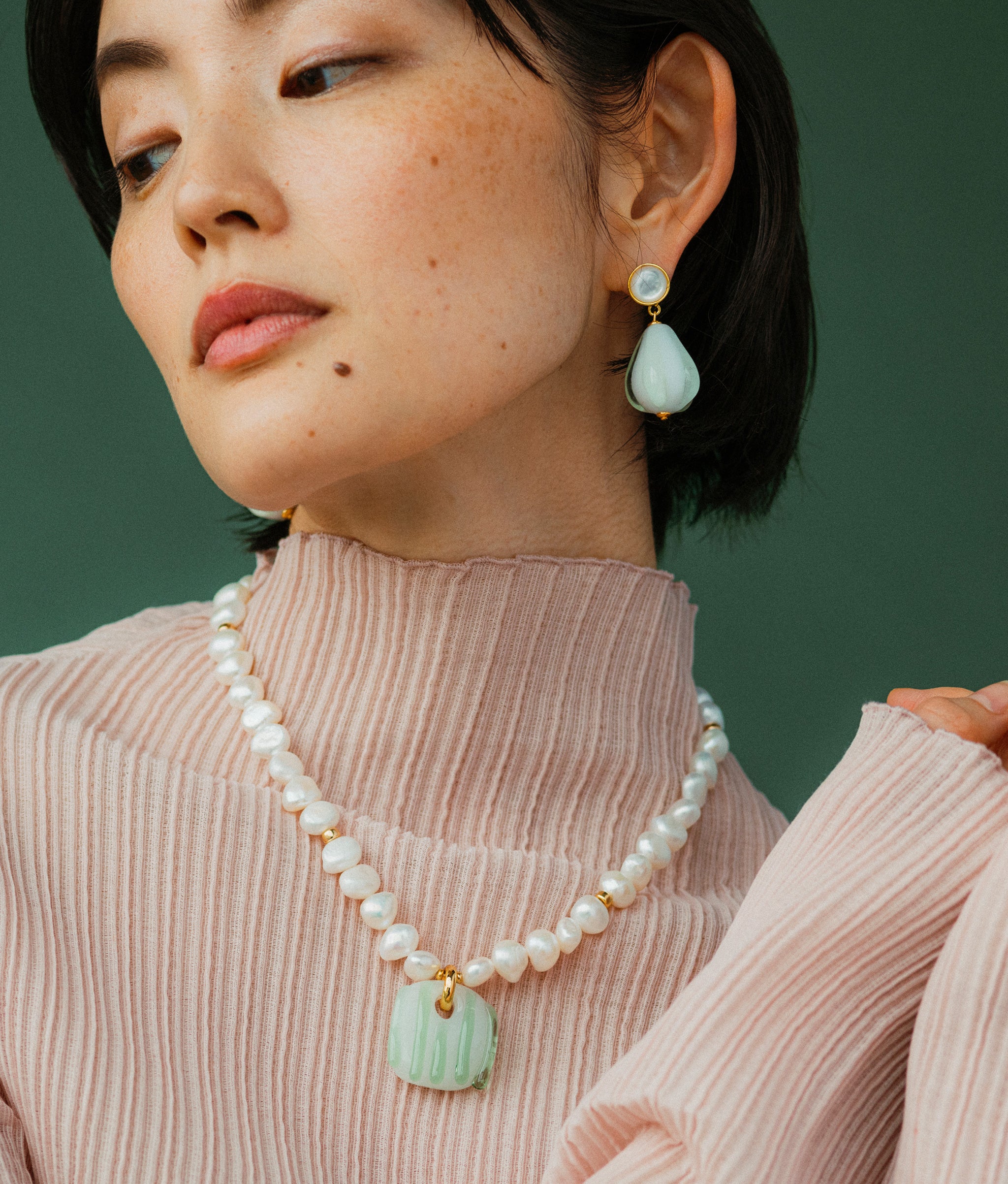 Model wears Sean Bean Earrings with Marine Glass Necklace on a green backdrop.