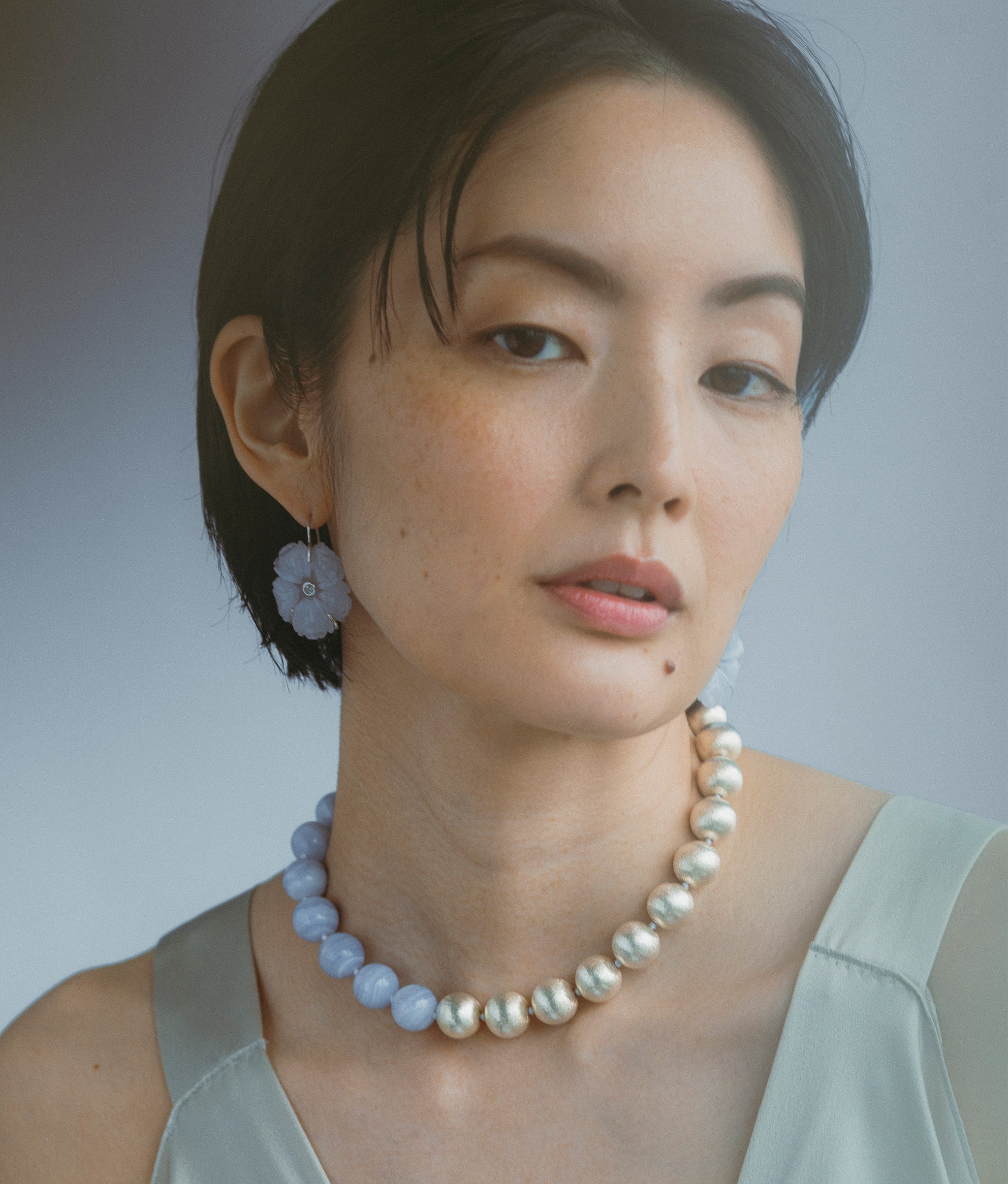 Model on a grey backdrop wears New Bloom Earrings and Silver Sky Collar