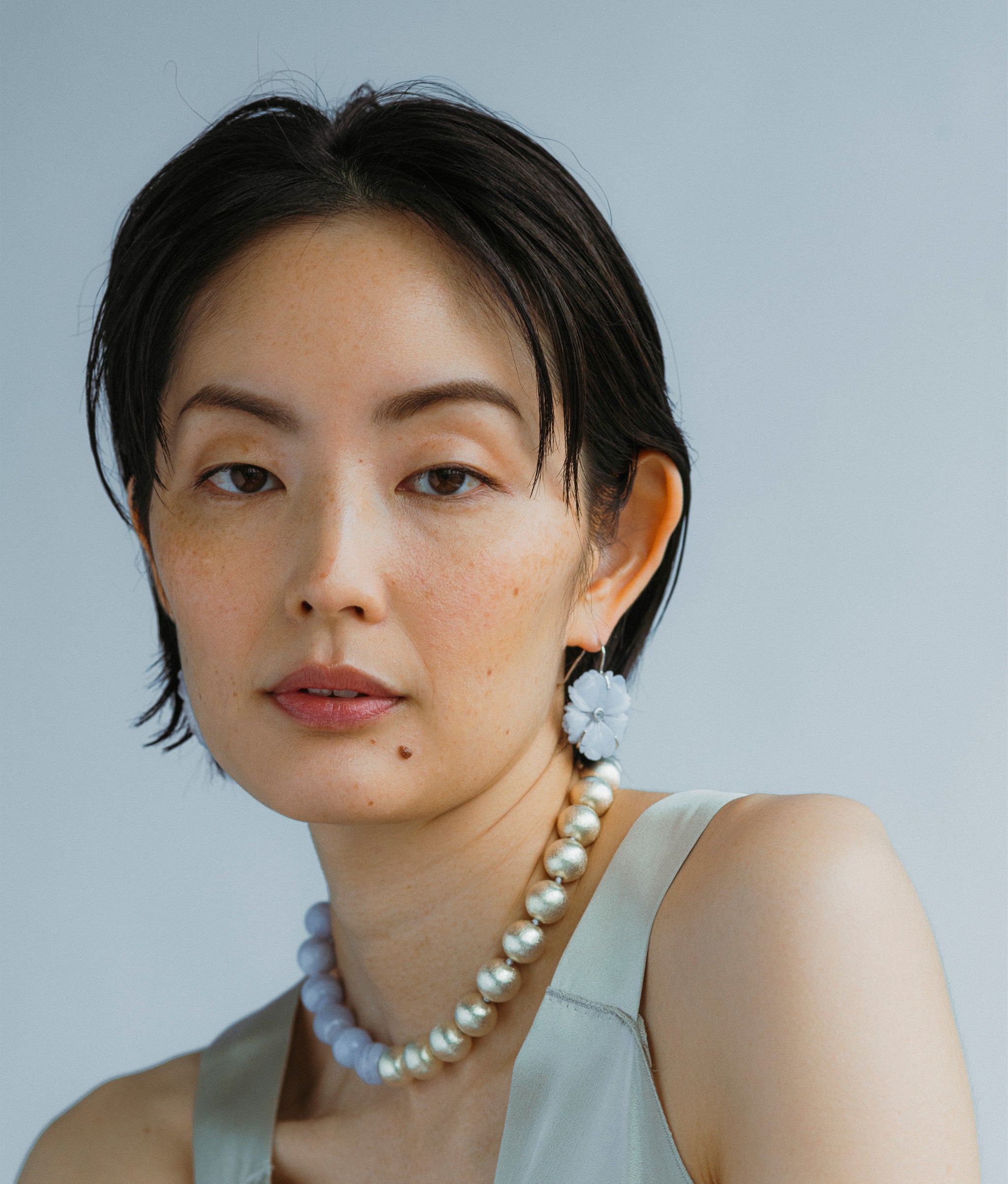 Model on a grey backdrop wears New Bloom Earrings and Silver Sky Collar