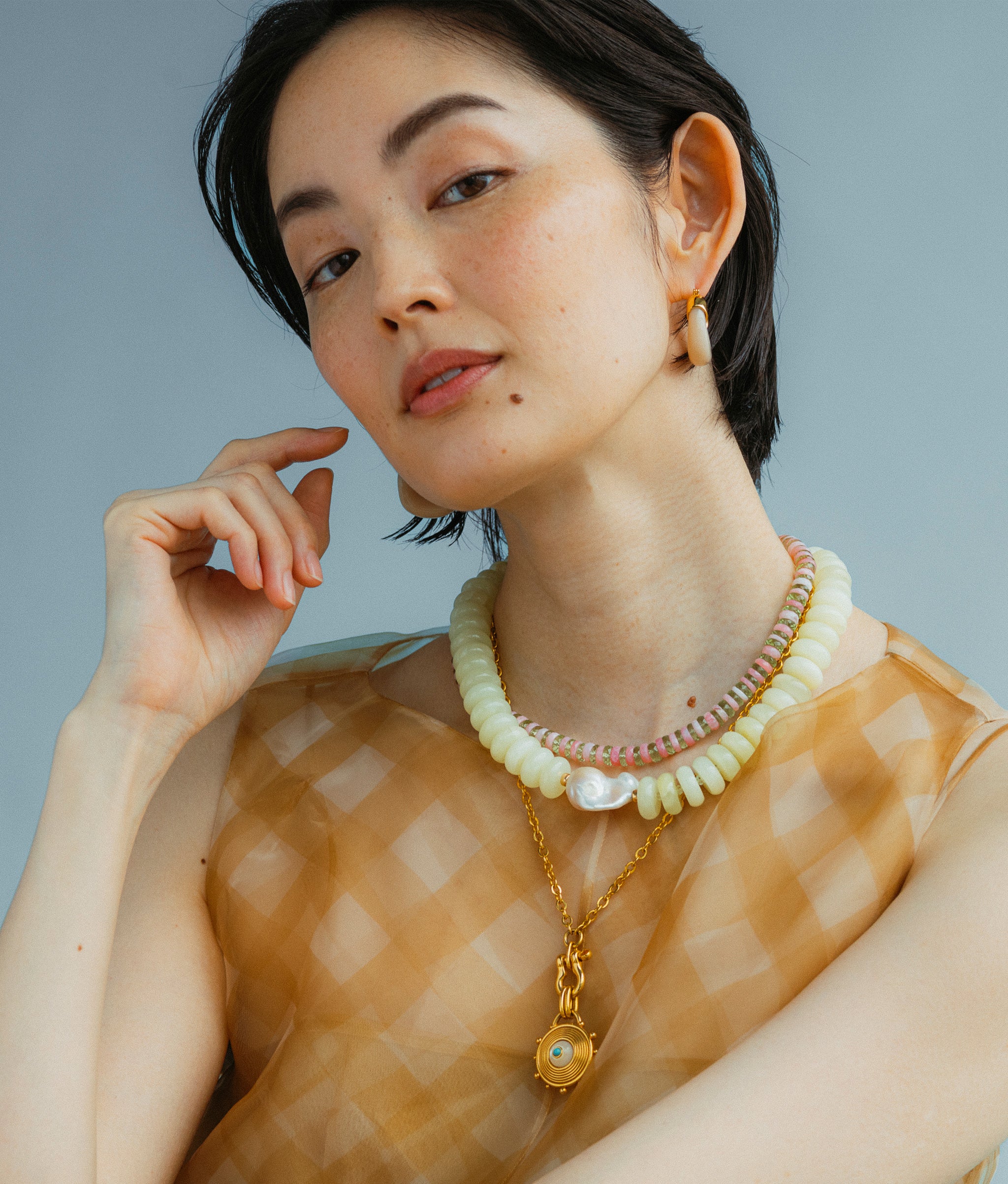 Close-up of model wearing Mini Organic Hoops in Dove featuring Tidal Pendant In Urchin overlayed with Santo Necklace Petal and Provence Necklace In Serpentine