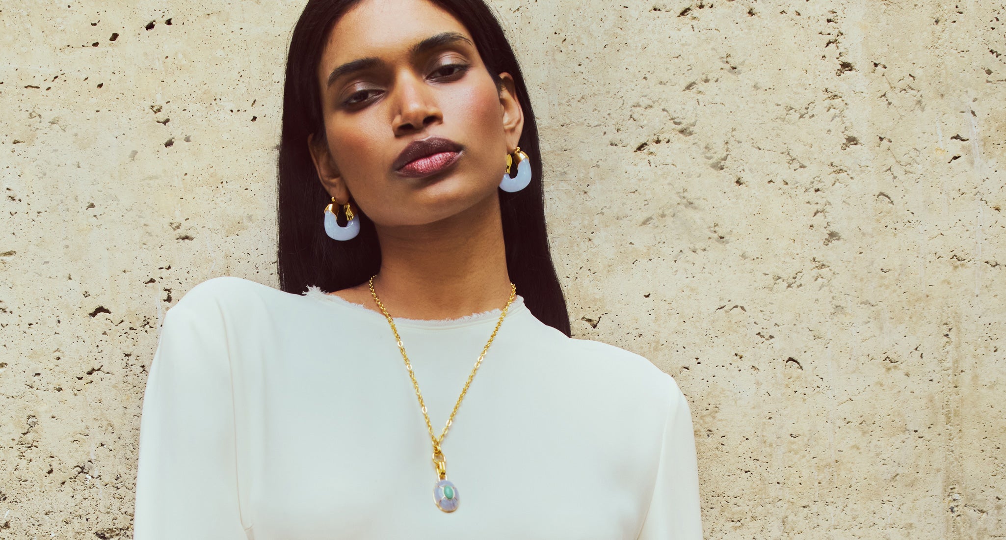 Model on stone backdrop wears white top with Organic Hoops in Blue Lace and Yucca Pendant Necklace