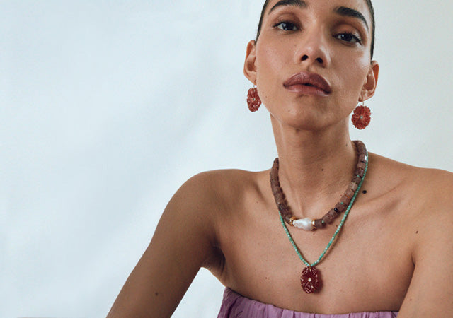 Model on grey backdrop wears strapless pink top with Royal Hawaiian and New Bloom Necklace and earrings.