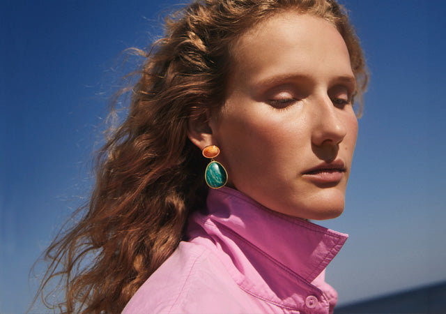 Model on blue sky wears pink coat with orange and aqua semiprecious stone earring