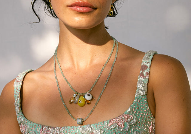 Model on grey backdrop wears brocade top with tiny aquamarine bead necklaces and charms