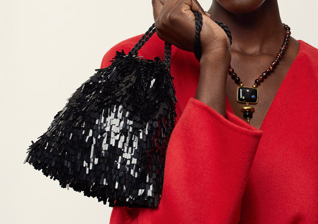 Model wears red coat with Constellation Pendant Necklace, holds up Gala Bag in Black