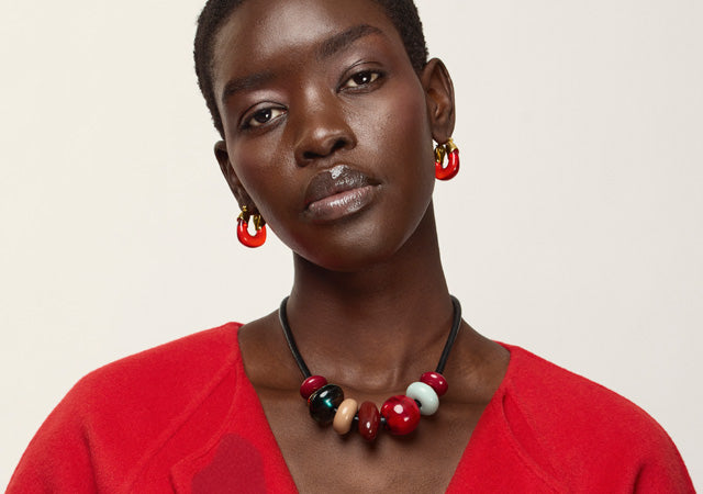 Model in red jacket wears Mini Organic Hoops in Cherry and Piedra Necklace