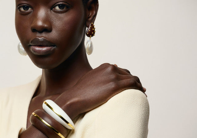 Model on tan backdrop wears cream blazer with Halo Cuffs and Orbit Earrings