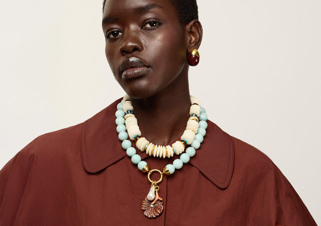 Model wears burgundy coat with Petra Collar, Desert Bloom Necklace and Toro Earrings
