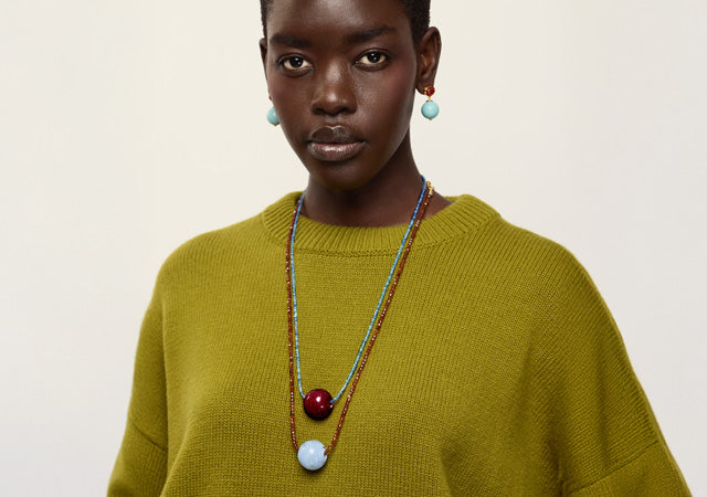 Model on grey backdrop wears chartreuse sweater with Umbria Earrings and Callisto Necklaces