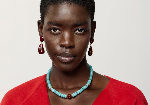 Model on grey backdrop wears red top with Satsuma Earrings and Hidden Stone Necklace