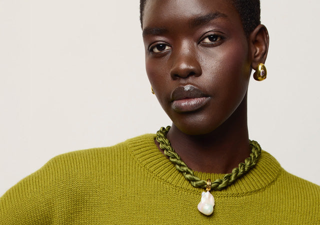 Model wears moss green sweater with Mini Arp Earrings in Gold and Woven Collar in Olive Branch