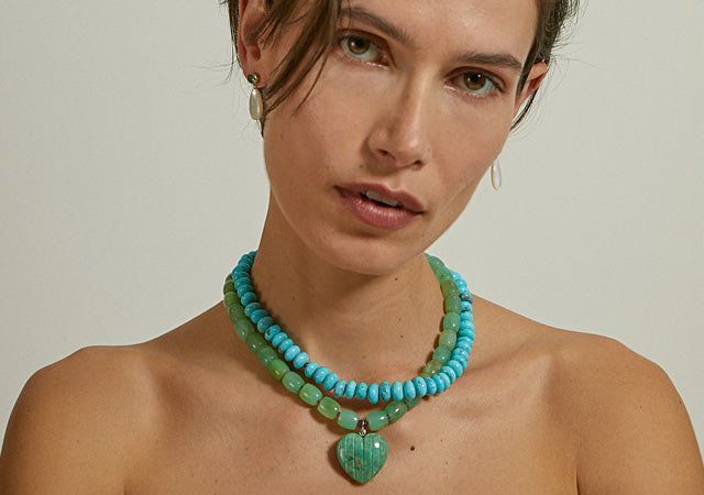 Model on grey backdrop wears blue and green beaded necklaces