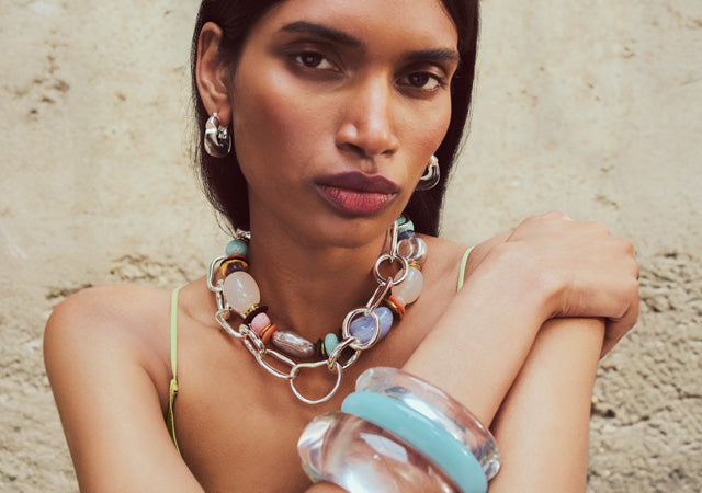 Model on tan stone backdrop wears Monument Collar, silver Porto Chain, and stack of resin bracelets