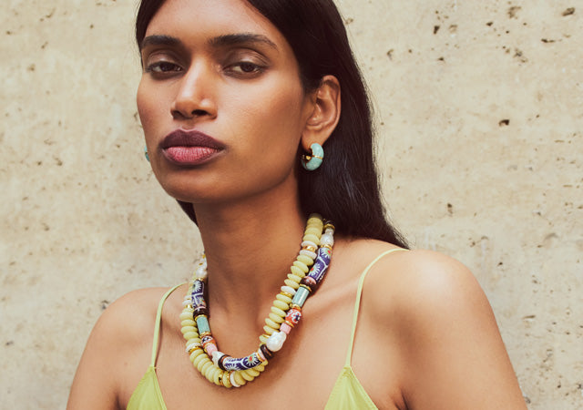 Model on tan stone backdrop wears Laguna and Souvenir Necklaces with Zellige Hoops