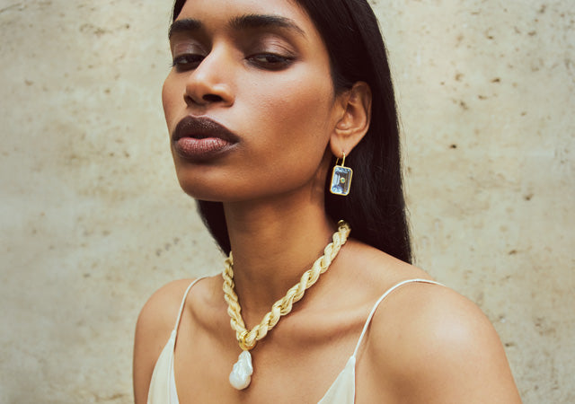 Model on stone backdrop wears Woven Collar in Sandbar and Tile Earrings
