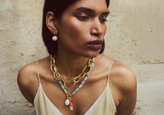Model on stone backdrop wears tank top with Cortez Necklace, Porto Chain and Comet Earrings