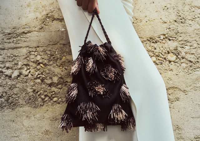 Model on stone backdrop wears white skirt and holds Gala Bag in Shooting Star
