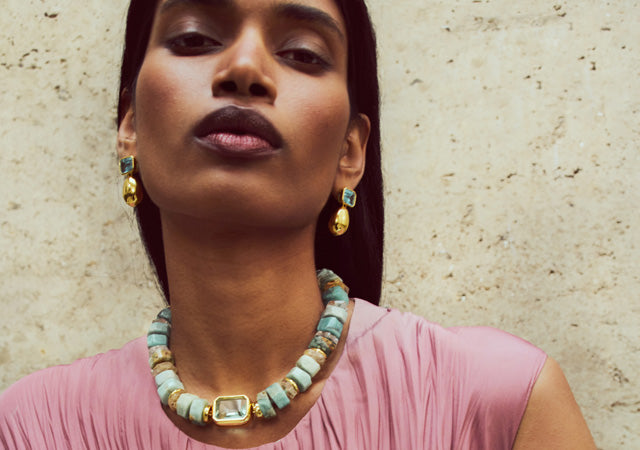 Model on stone backdrop wears pink top with Goddess Collar and Bean Earrings