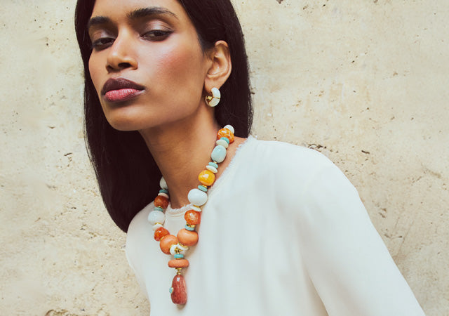 Model on tan stone backdrop wears white top with Andamento Necklace and Zellige Hoops