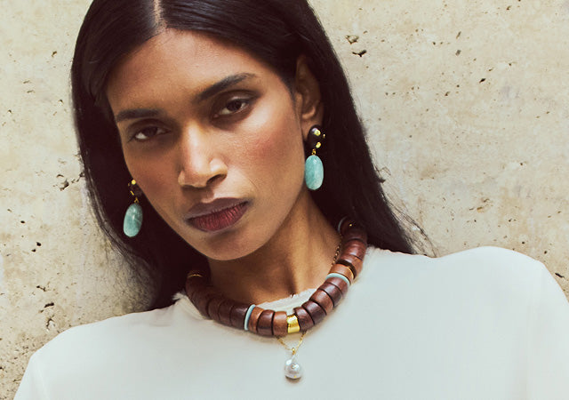 Model on tan stone backdrop wears white top with Nopales Earrings, Las Palmas Collar and Oasis Necklace