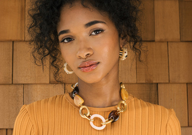 Model on wood shingle backdrop wears orange top with La Bomba Hoops and link necklace