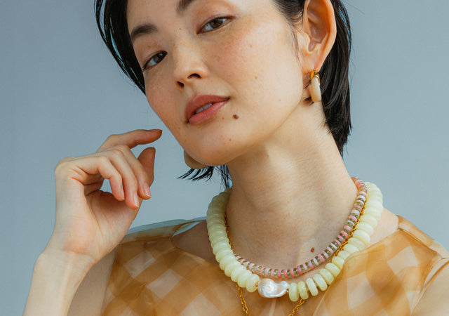 Model on blue backdrop wears jewels from FW24 collection