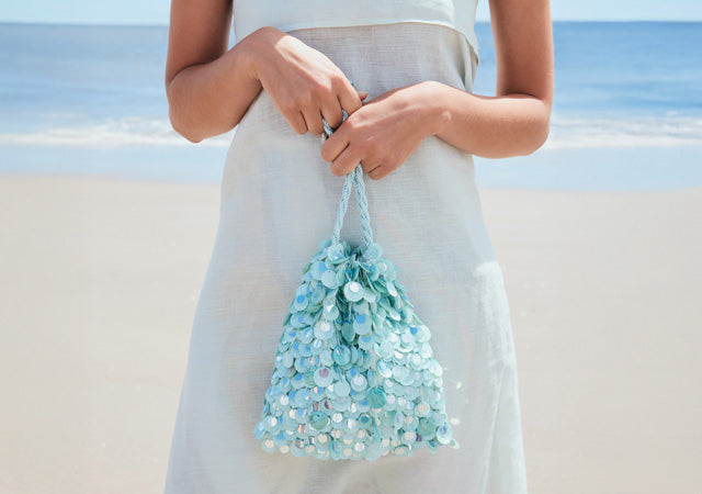 Model on beach wears light dress and holds Gala Bag in Aquamarine