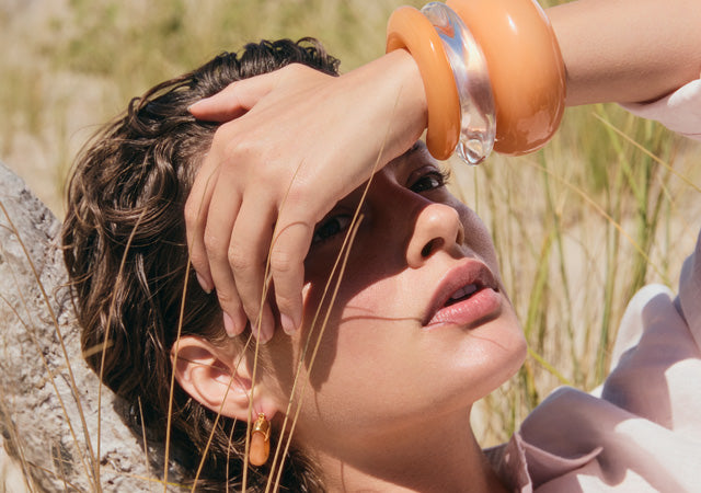 Model holds hand over face and wears stack of Arc and Ridge Cuffs, Mini Organic Hoops in Tangerine