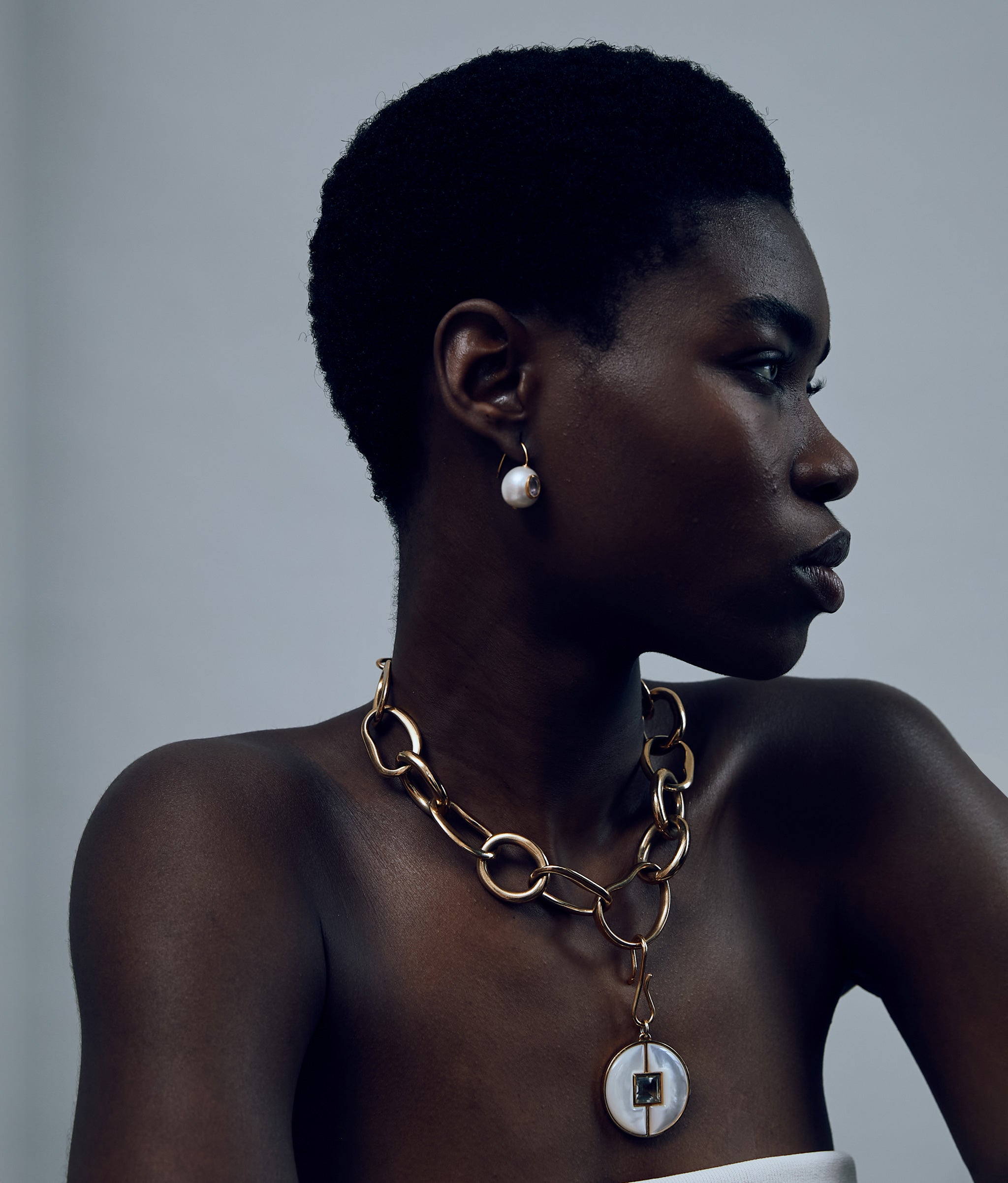 Model on grey background wearing Porto Chain with Porto Pendent in Mother-of-pearl and Pearl Pablo Earrings.