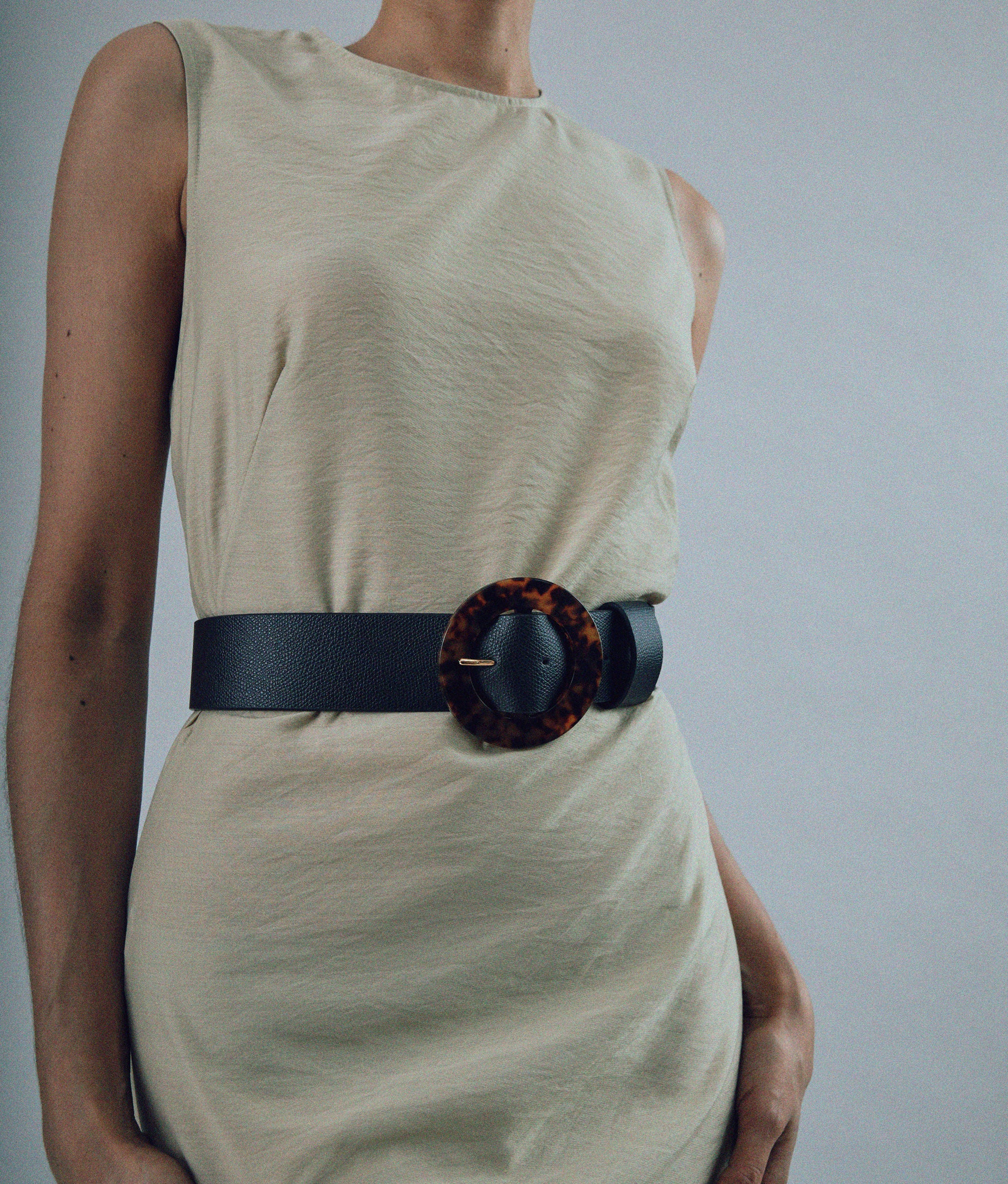 Our Louise Belt in Black leather, featuring an oversized round buckle in tortoiseshell resin styled on model.