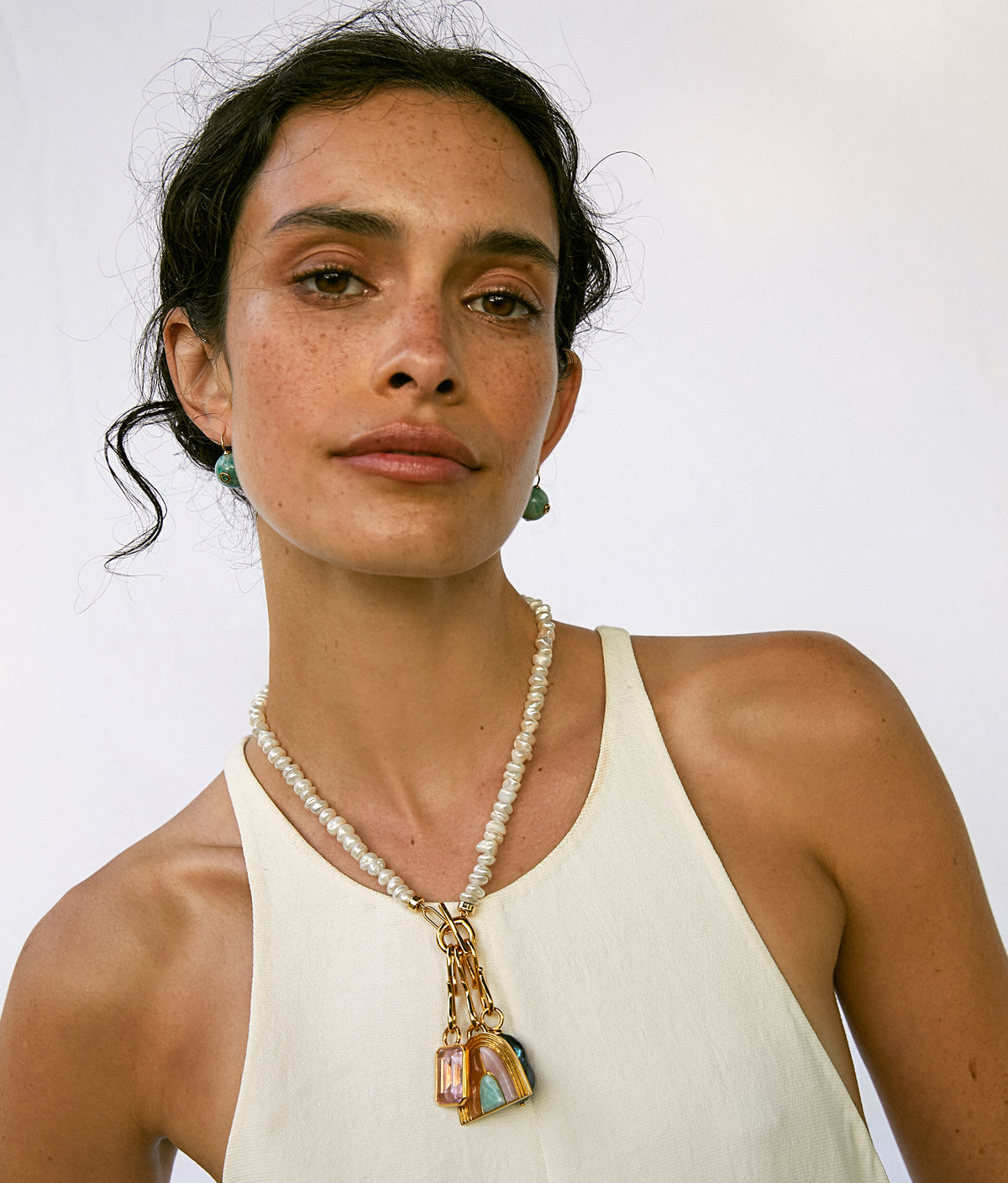 Model in white tank top wears Mood Necklace in Pearl with assorted charms and Comet Earrings.