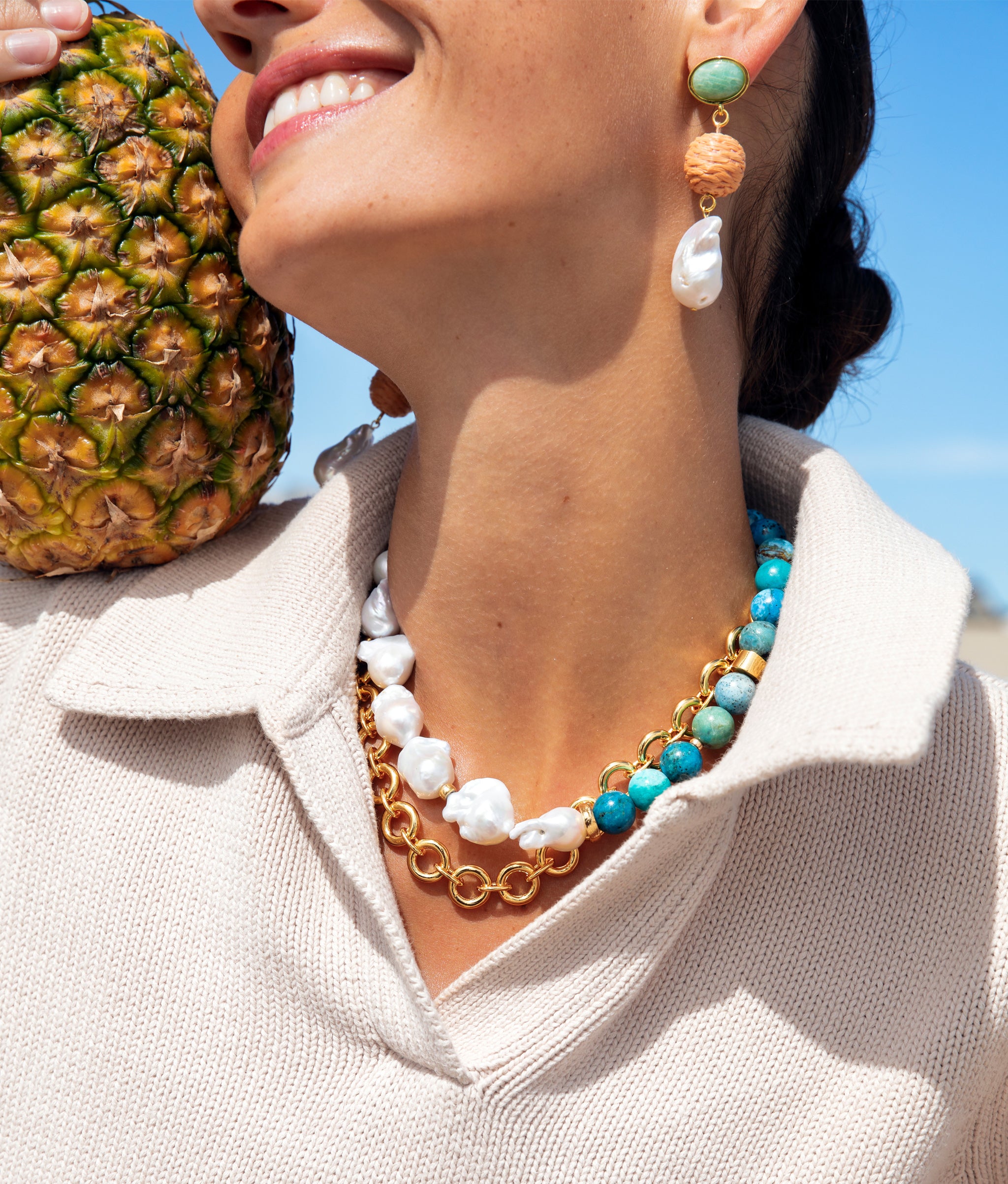 Close-up of model with a pineapple wearing Mood Necklace in Gold with Mandarina Drop Earrings and Formentera Necklace.