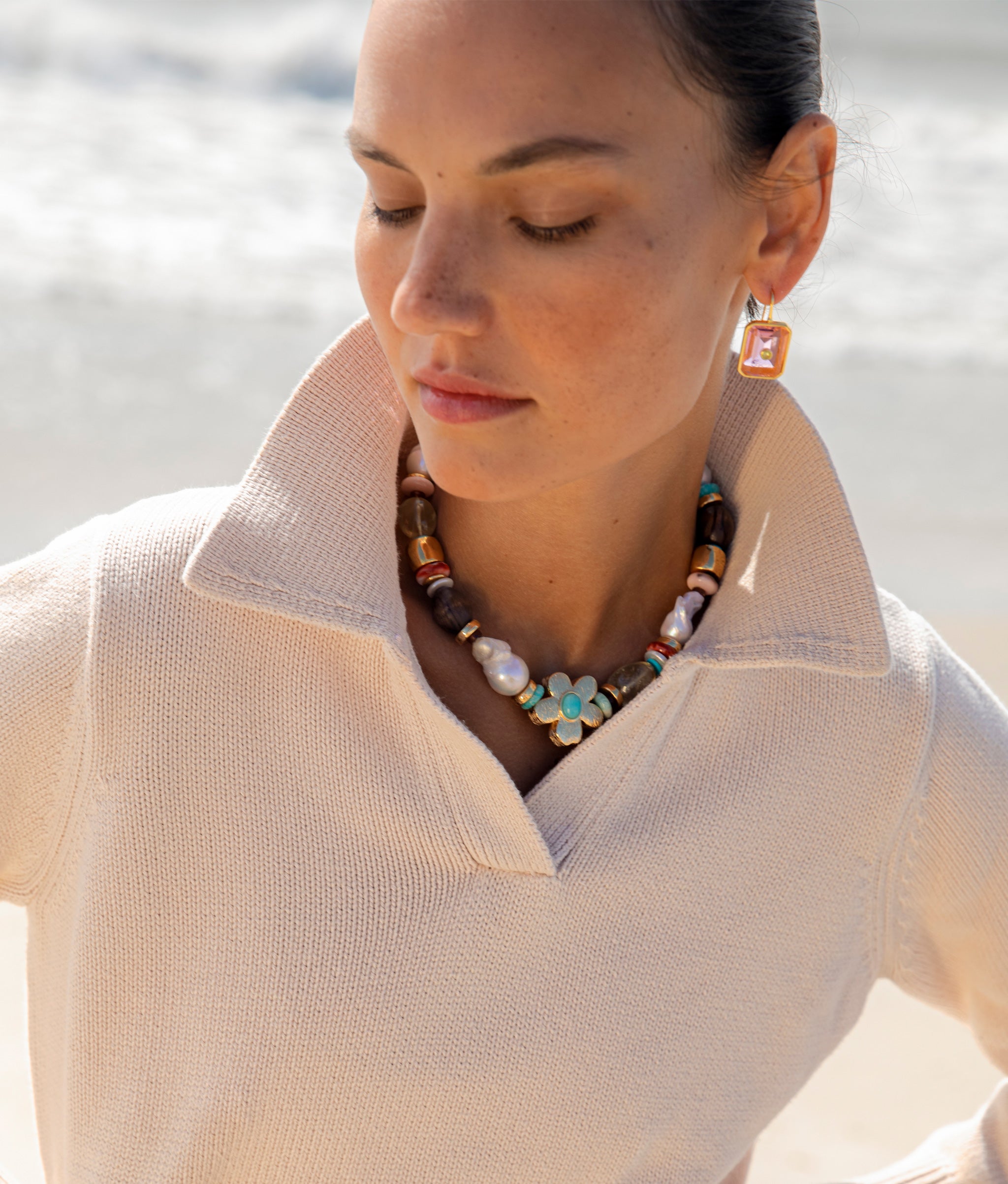 Close-up of model at the beach wearing the Tile Earrings in Pale Pink with the Mistflower Necklace in Apple.