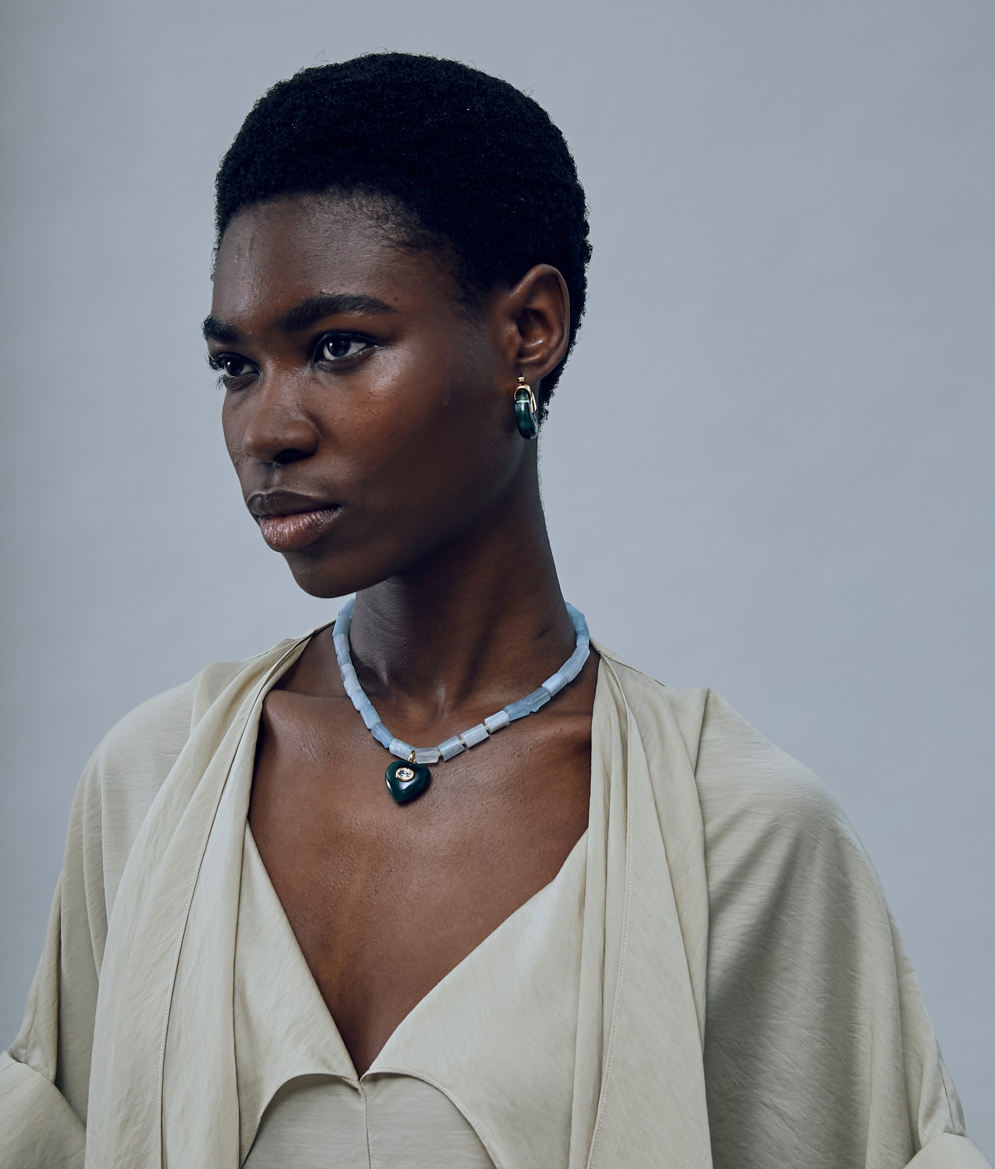 Close-up of model on grey background wearing the Infatuation Necklace in Jade with the Organic Hoops in Forest.