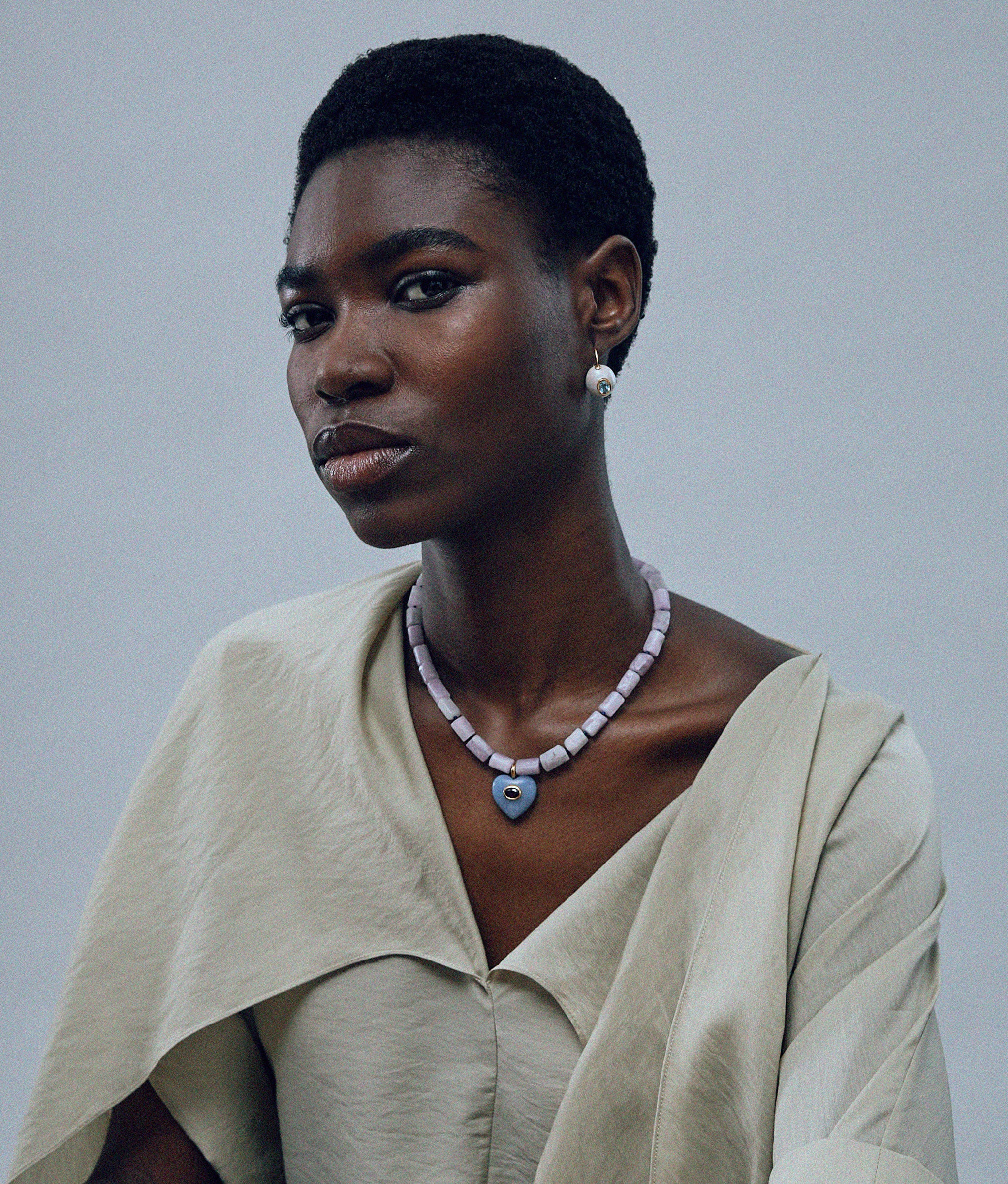 Model on grey background wearing the Infatuation Necklace in Angelite with the Pearl Pablo Earrings in Blue Topaz.
