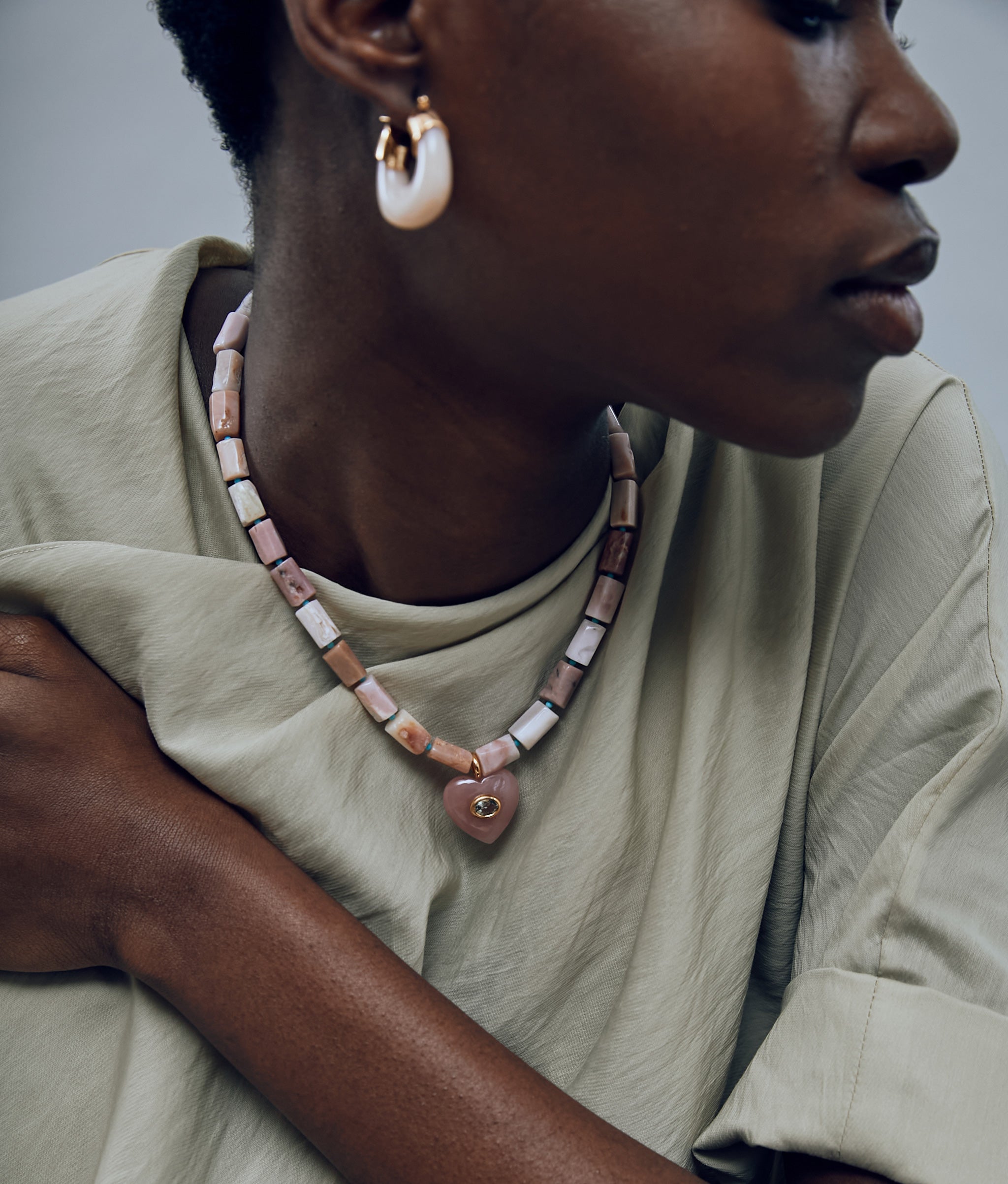 Model on grey background wearing the Infatuation Necklace in Guava with the Organic Hoops in Dove.