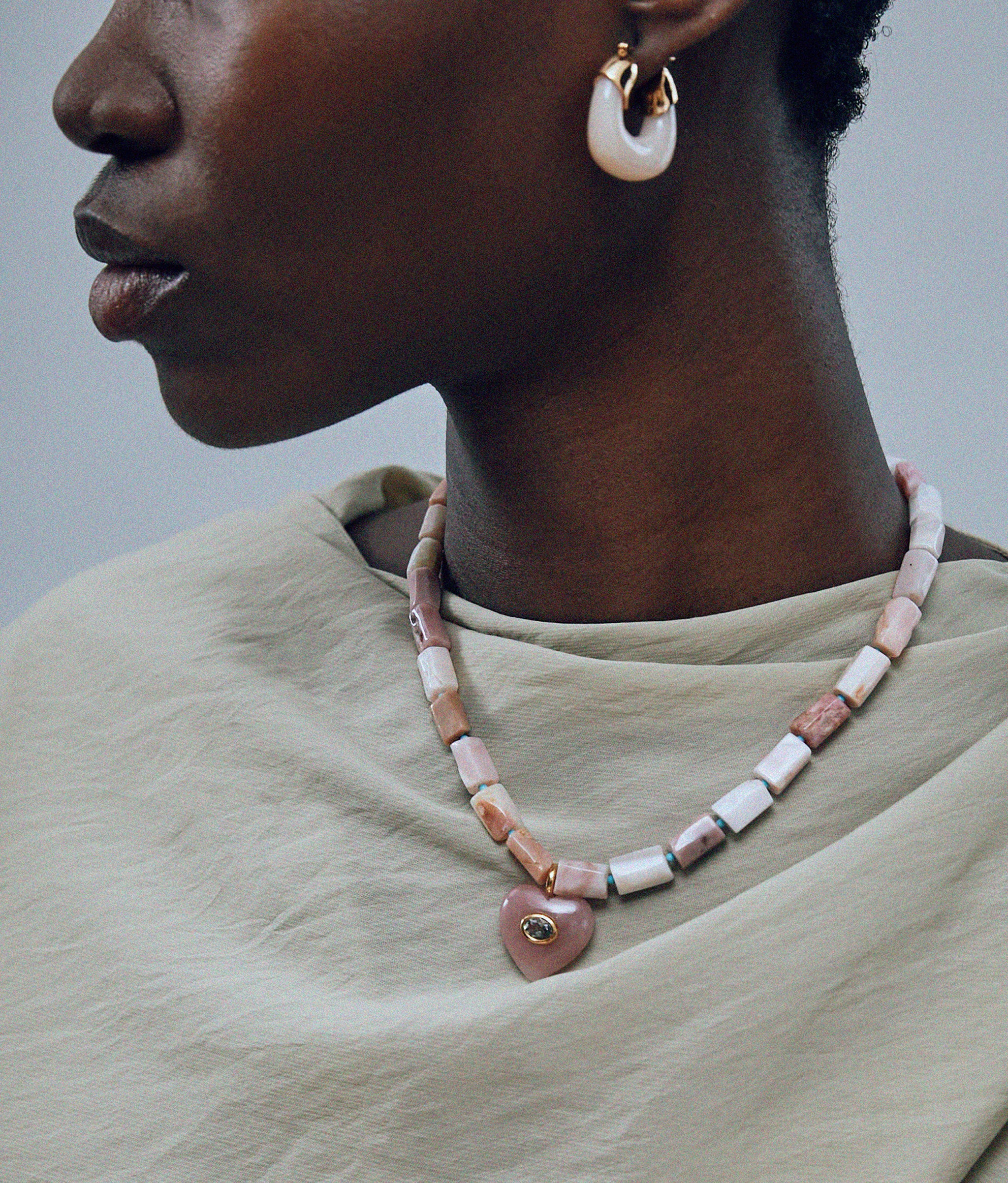 Close-up of model on grey background wearing the Infatuation Necklace in Guava with the Organic Hoops in Dove.