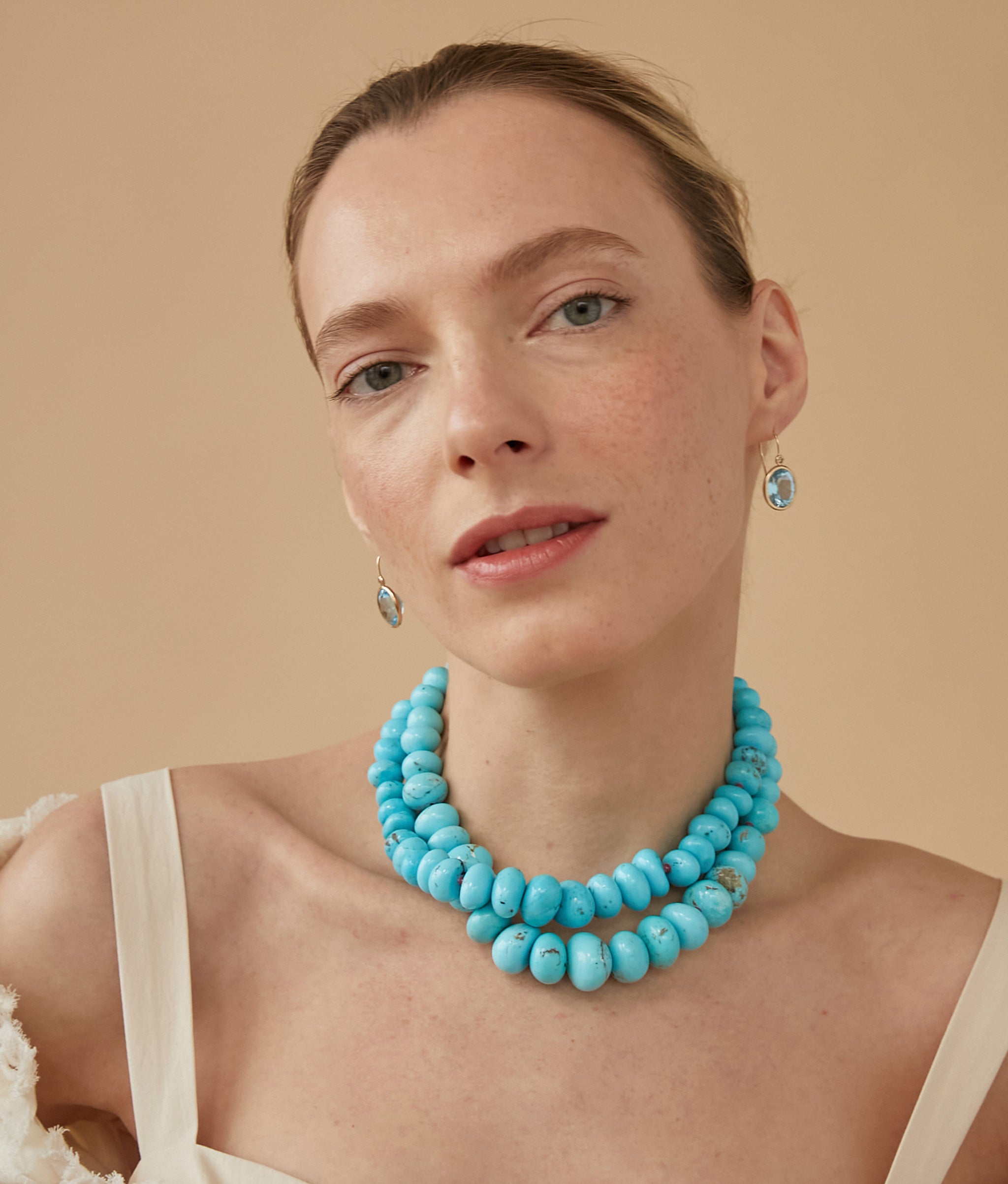 Model on tan backdrop wears cream strap top with two layered Large Graduated Turquoise & 14k Gold Necklaces. 