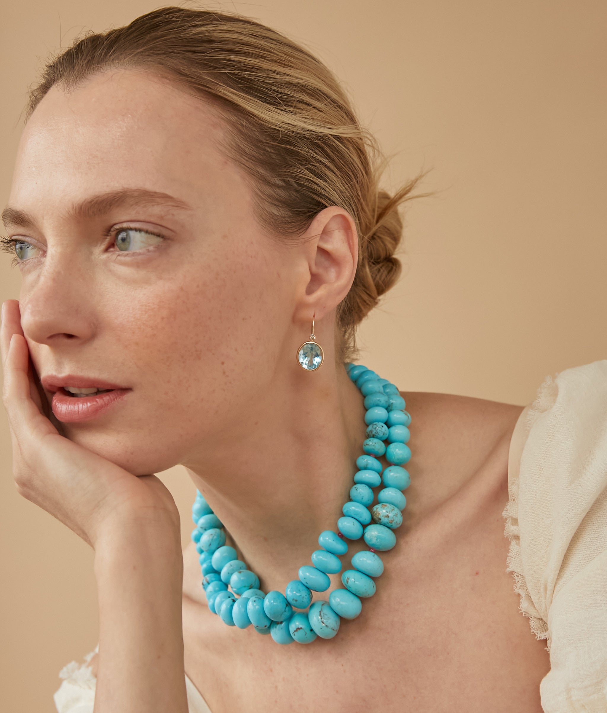 Model in profile on tan backdrop wears cream top with two layered Large Graduated Turquoise & 14k Gold Necklaces. 