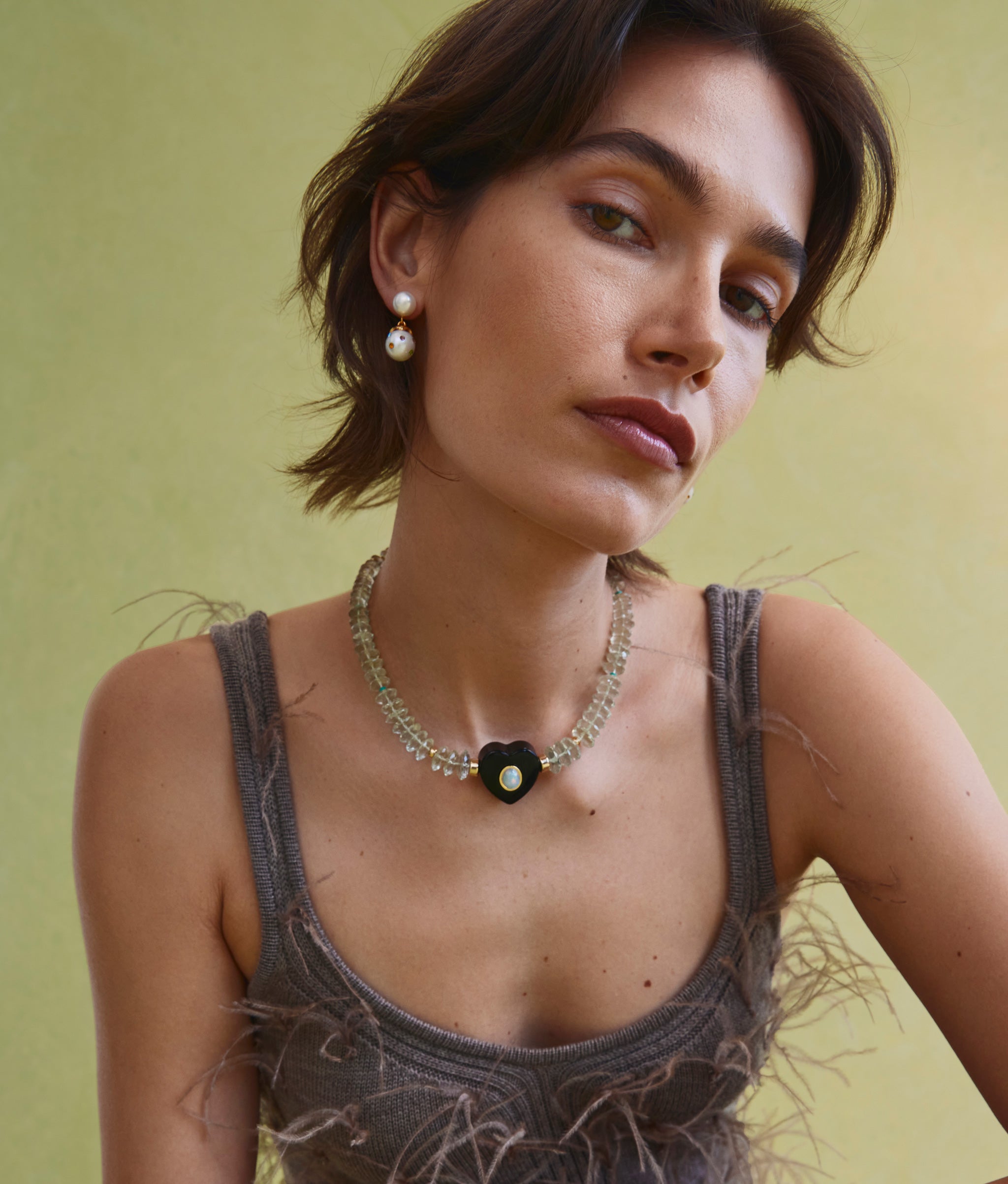 Model on green backdrop wears brown feather tank with Gemini Collar in Meadow and Confetti Drop Earrings in White.