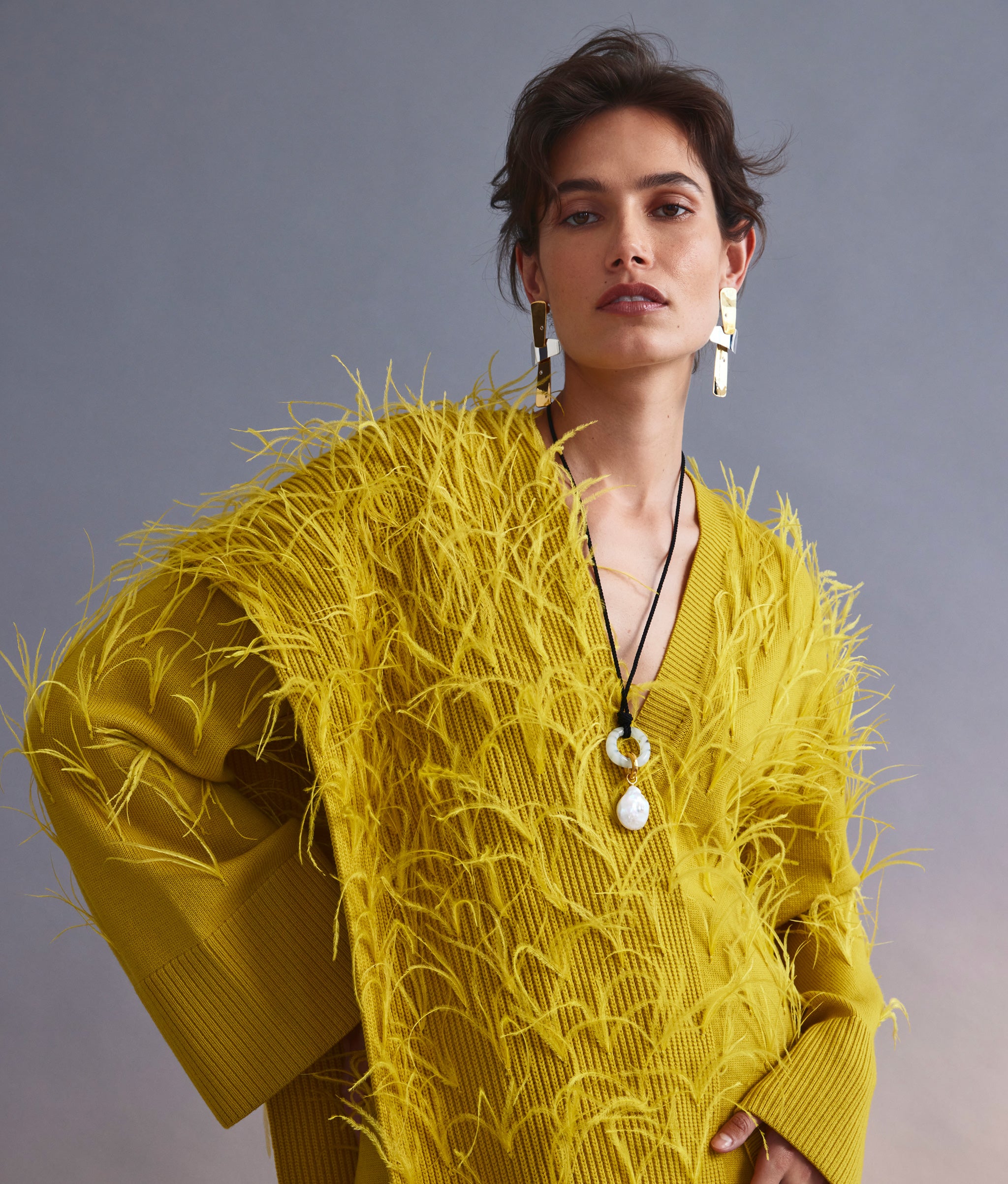 Model on grey backdrop wears yellow feather sweater with Ernesto Earrings in Mixed Metal and Sun at Noon Necklace.